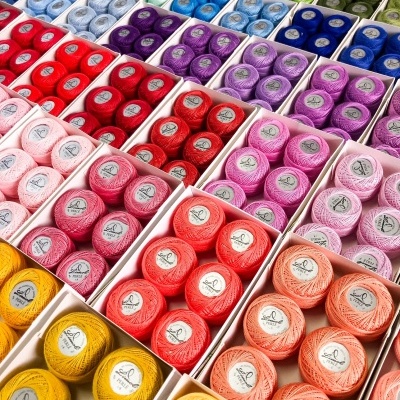 Caixas com novelos de linha de algodão coloridos organizados por cores.