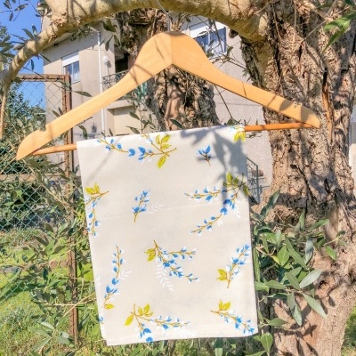 Lenço branco com flores azuis e folhas verdes pendurado num cabide de madeira numa árvore