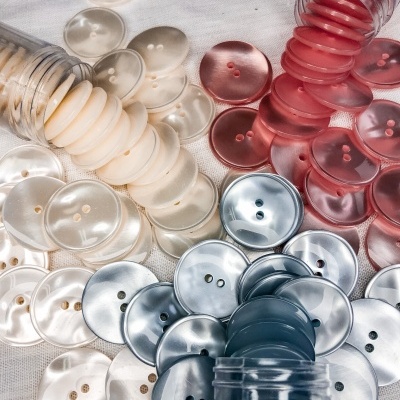 Botões redondos coloridos em plástico sobre tecido branco, com vários frascos transparentes