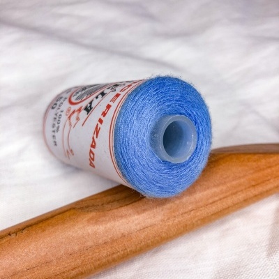 Carretel de linha azul com rótulo com texto, sobre tecido branco e madeira