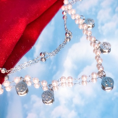 Colar prateado com contas tipo pérola e pendentes redondos sobre espelho refletindo céu azul