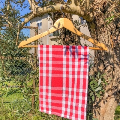 Pano de cozinha xadrez vermelho e branco pendurado em cabide de madeira numa árvore ao ar livre