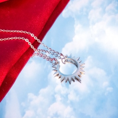 Colar prateado com pendente circular pontiagudo sobre fundo de céu com nuvens e tecido vermelho