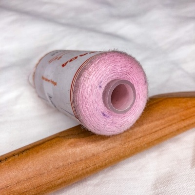Carretel de linha cor-de-rosa sobre objeto de madeira clara em tecido branco