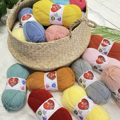 novelos de lã coloridos com etiquetas dentro e fora de um cesto de palha sobre chão branco