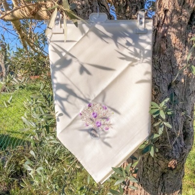 Pano branco com bordado de flores roxas pendurado numa árvore
