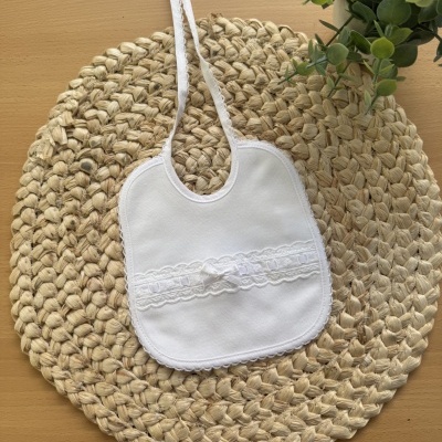 Babete branco com renda e laço sobre base de palha clara
