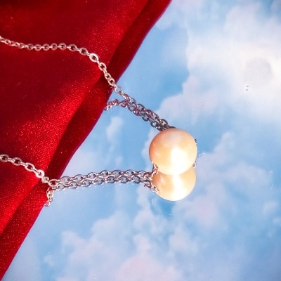 Colar com pérola branca e corrente prateada sobre reflexo do céu e tecido vermelho