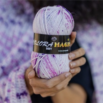 Novelo de lã branca com manchas roxas para bebé com etiqueta preta e mãos a segurá-lo