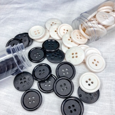 Botões redondos brancos e pretos com quatro furos em tecido branco.