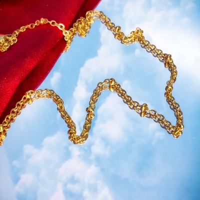 Colar dourado sobre fundo azul com nuvens e tecido vermelho