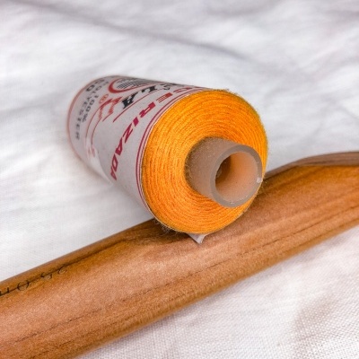 carretel de fio amarelo com etiqueta e ferramenta de madeira sobre tecido branco