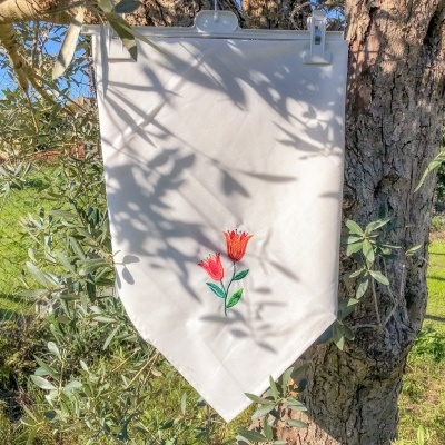 Bandeira branca com bordado de flores vermelhas pendurada numa árvore