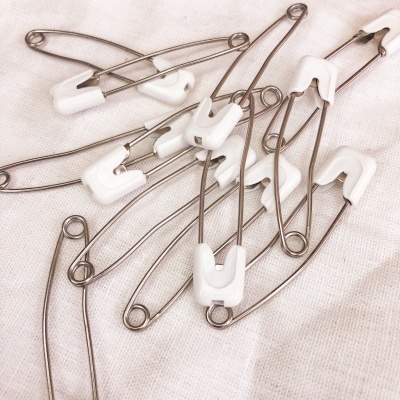 Alfinetes de segurança metálicos com proteção branca sobre tecido branco