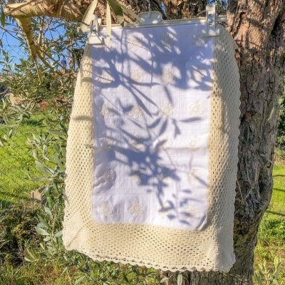 Manta branca com bordado dourado e renda bege pendurada numa árvore