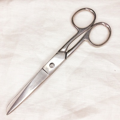 Tesoura metálica com cabo em argola sobre tecido branco