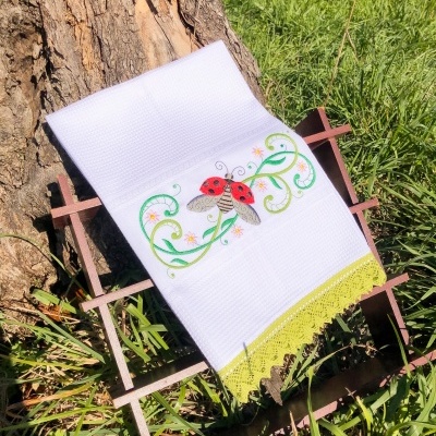 Toalha branca com bordado de joaninha sobre suporte de madeira na relva