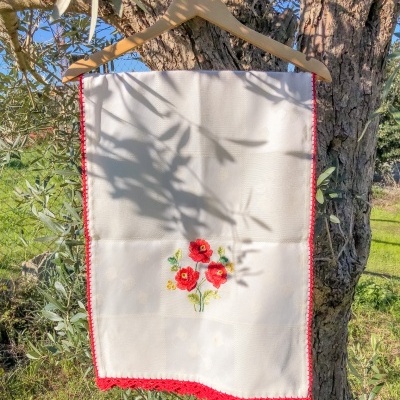 Toalha branca bordada com flores vermelhas pendurada num cabide de madeira numa árvore