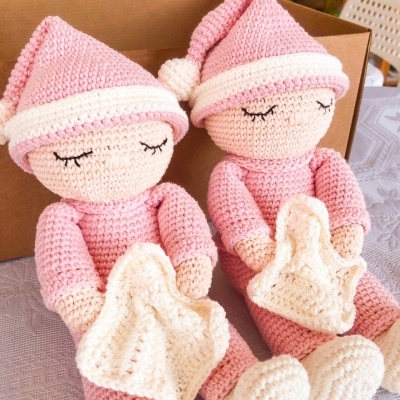 Dois bonecos de croché cor-de-rosa com toucas e mantas brancas