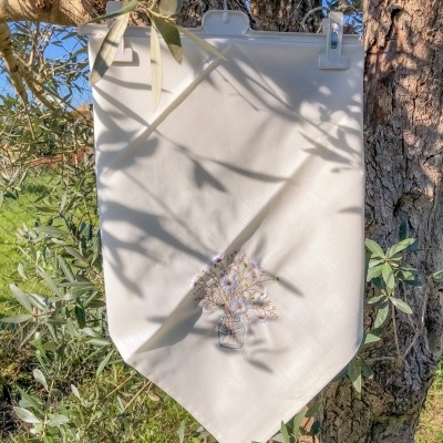 Pano decorativo branco com bordado de jarro com flores pendurado numa árvore