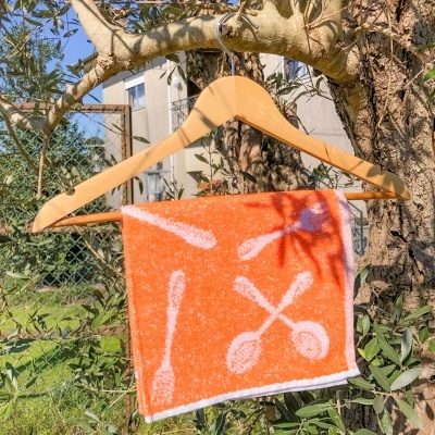 Toalha laranja com padrão de colheres pendurada em cabide de madeira numa árvore