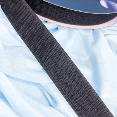 Fita de velcro preta sobre tecido azul claro com rolo de fita preta ao lado