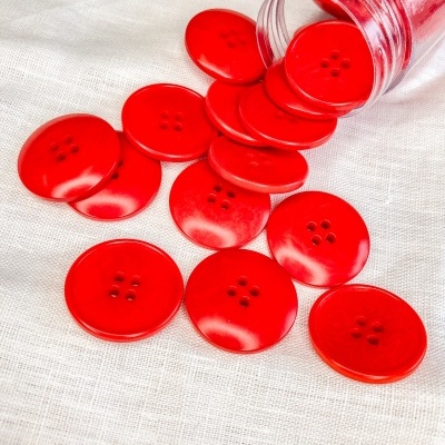 Botões vermelhos grandes com quatro orifícios em tecido branco e frasco plástico