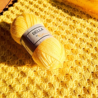 Novelo de fio amarelo com etiqueta sobre manta amarela texturizada em madeira