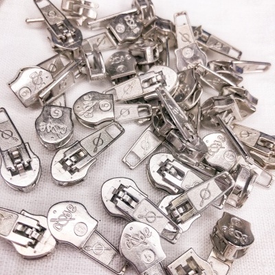 Puxadores metálicos prateados para fechos éclair com inscrições e símbolos