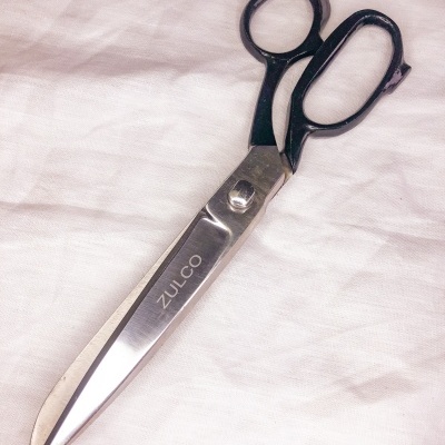 Tesoura grande metálica com cabo preto sobre tecido branco