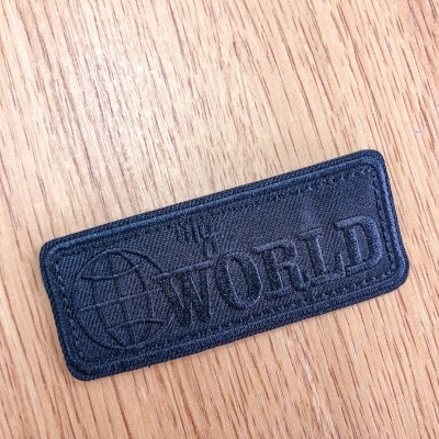 Etiqueta preta bordada com orelho e palavra WORLD sobre madeira clara