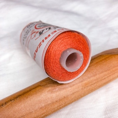 Bobine de linha de costura laranja com etiqueta e ferramenta de madeira