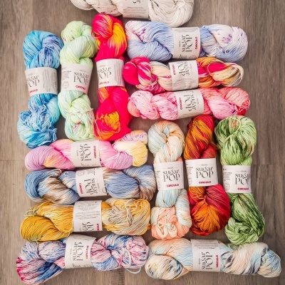 Conjunto de novelos de lã coloridos com etiquetas SUGAR POP CIRRADO sobre chão de madeira