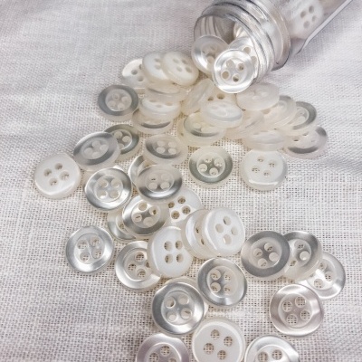 Botões redondos brancos com brilho perolado e borda prateada sobre tecido branco