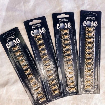 Embalagens pretas com presilhas metálicas douradas para cabelo sobre tecido branco