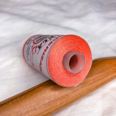 Rolo de linha cor de salmão com etiqueta e carretel cinzento sobre madeira clara e tecido branco