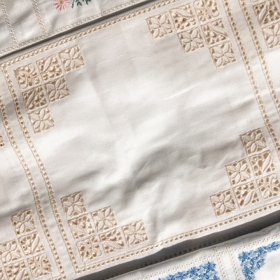 Pano de mesa branco com bordados geométricos bege e outras peças bordadas coloridas