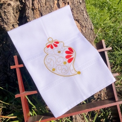 Toalha branca com bordado colorido pendurada em suporte de madeira perto de árvore