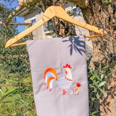 Toalha cinzenta com bordado de galo pendurada em cabide numa árvore