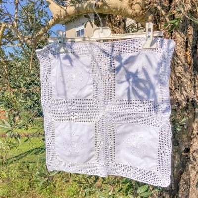 Guarda de croché branca quadrada pendurada numa árvore numa zona ajardinada