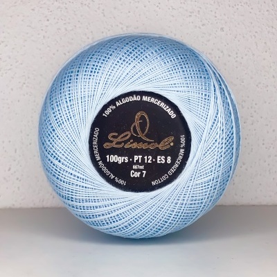 Bola de linha azul clara com etiqueta preta com texto sobre superfície branca e parede bege