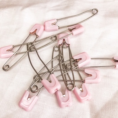 Alfinetes de segurança metálicos com tampas cor-de-rosa sobre tecido branco