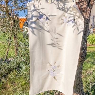 Toalha branca com bordados florais pendurada ao sol junto a árvore