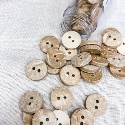 Botões de madeira clara com dois buracos sobre tecido branco e em recipiente plástico
