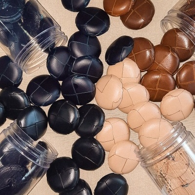 Bolas de couro preto, castanho e bege espalhadas e em frascos de plástico transparente.