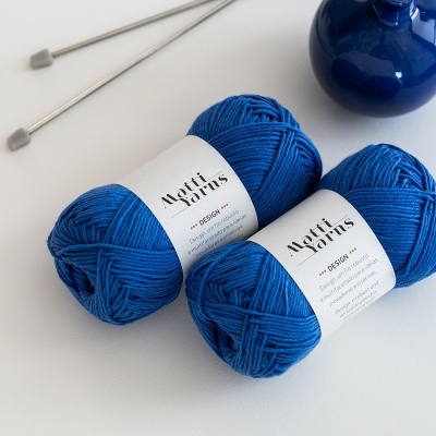 Dois novelos de lã azul royal com etiquetas da marca Matti Yarns, agulhas de tricô e um vaso azul escuro