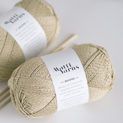 Novelos bege claro de fio Matti Yarns Whisper com etiqueta branca e paus de madeira ao fundo