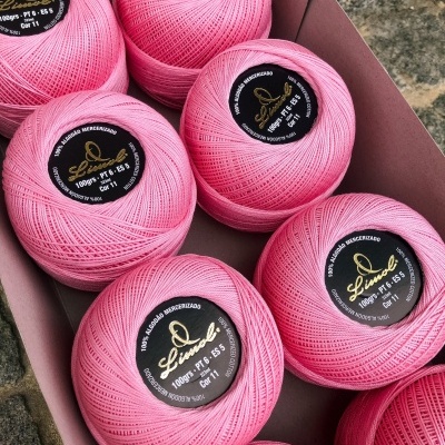 Novelos de linha cor-de-rosa com rótulos pretos e dourados dentro de caixa de cartão.