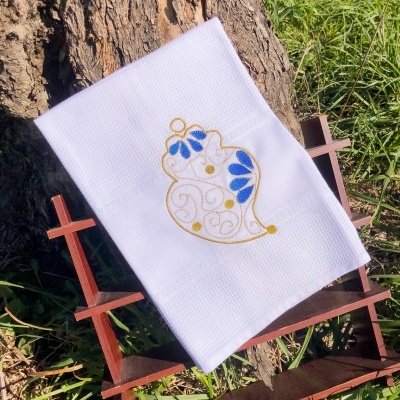 Toalha branca com bordado decorativo em dourado e azul numa estrutura de madeira ao ar livre