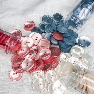 Botões redondos de plástico em vermelho, azul e branco perolado, com dois furos, em tecido branco